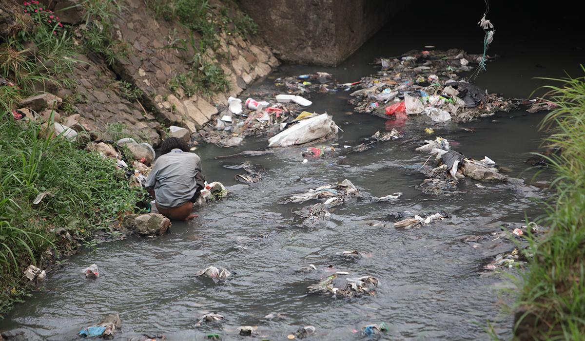 In lack of a toilet, a young man in Bandung relieves himself in a garbage-filled creek
